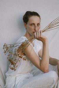 Portrait of woman holding flowering plant against white background