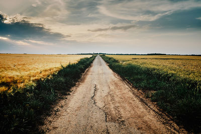 Dirt road amidst field against sky