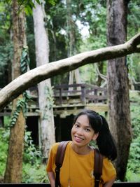 Portrait of young woman standing by tree trunk