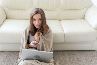 Young woman using phone while sitting on sofa at home