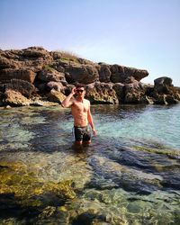 Shirtless young man standing in sea against clear sky during sunny day