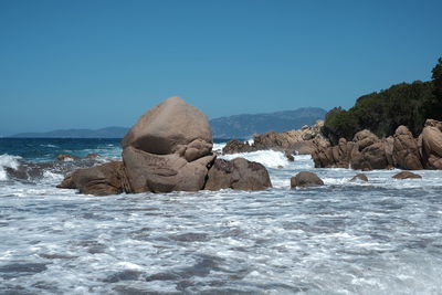 Rocks in sea against clear blue sky