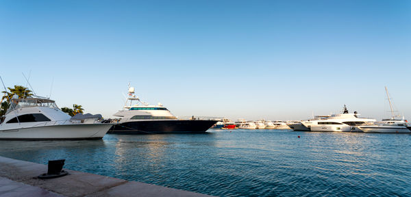 Boats moored in sea against clear blue sky