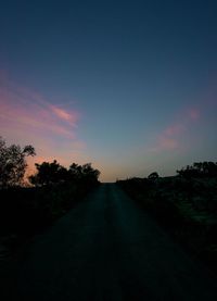 Empty road along silhouette trees at sunset