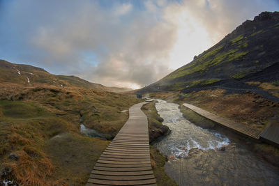 Narrow footpath leading towards mountains against sky