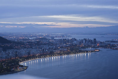 High angle view of illuminated city by sea against sky