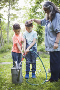 Grandmother looking at grandsons filling watering cans from garden hose in back yard