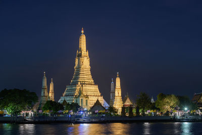 Illuminated temple building by river against sky at night