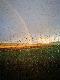 Close-up of raindrops on window against sky