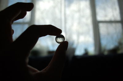 Cropped hand holding bead against window at home