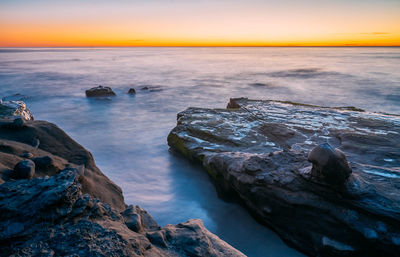 Rocks in sea against sky during sunset