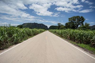 Empty road amidst field against sky