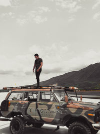 Man standing on car against sky