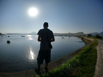 Rear view of man standing by sea against clear sky during sunny day