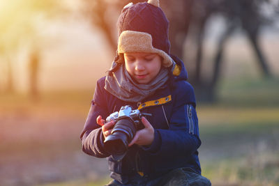 Boy holding camera on field 