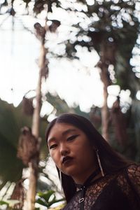 Low angle portrait of young woman standing against sky