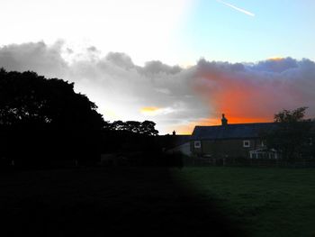 Silhouette trees and houses on field against sky during sunset