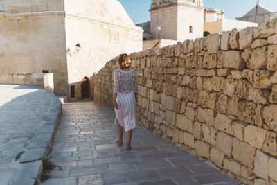 Rear view of woman walking by stone wall