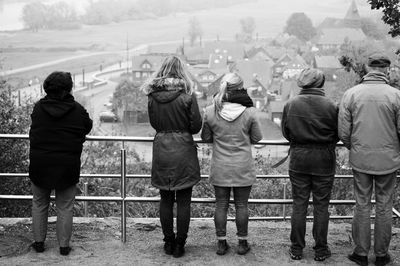 Rear view of people in warm clothes standing by railing in town