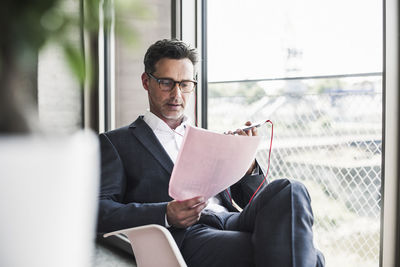 Businessman reading documents and speaking notes on smartphone