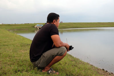 Side view of an indonesian young man squatting on the field near the lake