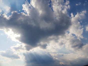 Low angle view of sunlight streaming through clouds