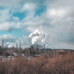 Smoke emitting from factory against cloudy sky
