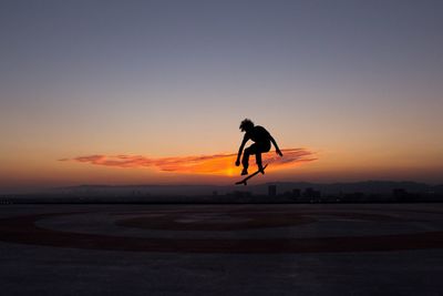 Full length of silhouette man performing skateboard stunt against orange sky