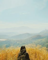 Rear view of woman standing amidst grass against mountains