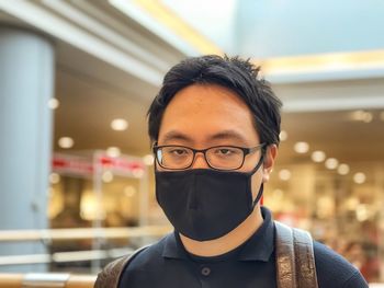 Portrait of young man wearing eyeglasses and face mask against neon lights inside mall.