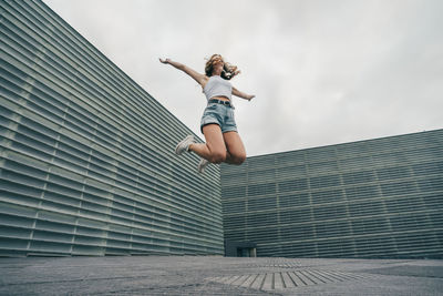 Carefree woman with arms outstretched jumping against wall