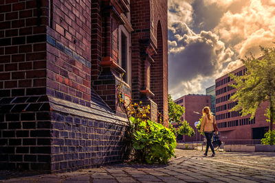 Woman walking on cobblestone street in city against sky