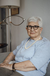 Smiling senior woman wearing eyeglasses sitting on sofa at home