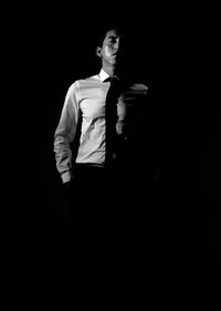 Portrait of young man standing against black background