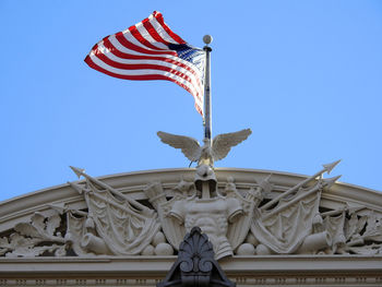 Low angle view of statue and flag against blue sky