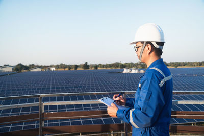 Side view of man holding mobile phone against blue sky