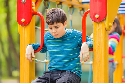 Sad and bored teen boy sitting on colorful playground in summer