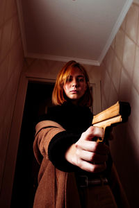 Portrait of beautiful woman pointing gun at home