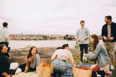 Cheerful friends enjoying by lake during picnic at weekend