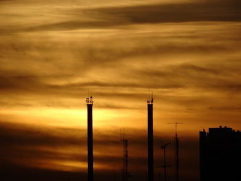 Silhouette of factory against cloudy sky during sunset