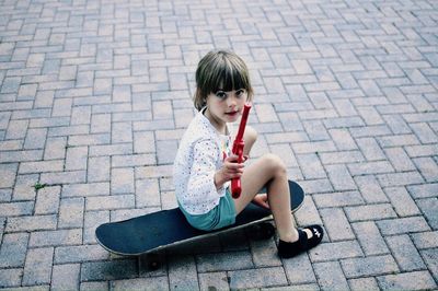Portrait of girl holding toy gun while sitting on skateboard