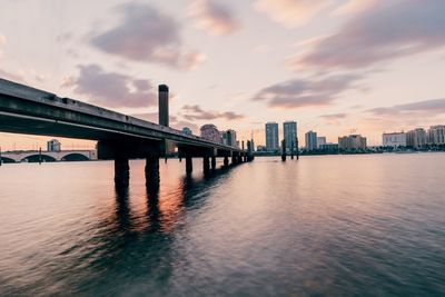 Bridge over river against sky during sunset in city