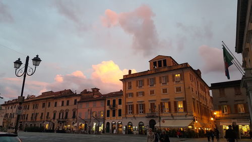 People walking on street amidst buildings in city at sunset