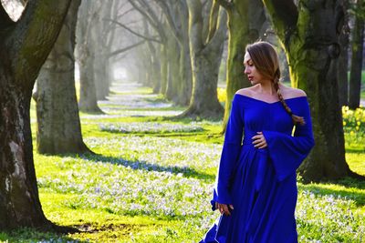Woman in blue dress standing on field amidst trees