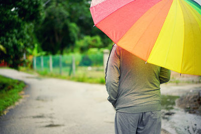 Rear view of person holding umbrella while standing on wet road during rainy season