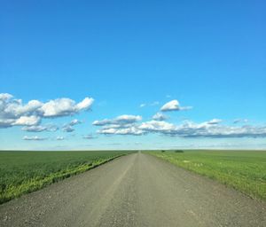 Road amidst field against blue sky