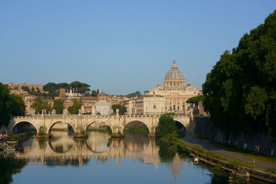 Arch bridge over river by buildings against clear blue sky