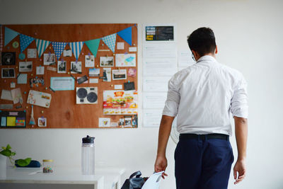 Rear view of man standing against wall at home