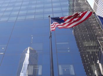 Low angle view of american flag against one world trade center reflection on glass building