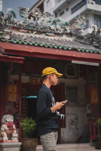 Side view of man holding mobile phone standing outside temple